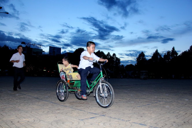 Hai con đạp xích lô nhí dưới sự “giám sát” của cha - Ảnh: Trung Tân