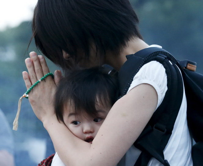 Người mẹ ẵm theo con đi cầu nguyện sáng 6-8 tại công viên Tưởng niệm Hòa bình, nơi đặt đài Tưởng niệm Hòa bình quốc gia Hiroshima dành cho các nạn nhân trong vụ ném bom 70 năm trước - Ảnh: Reuters