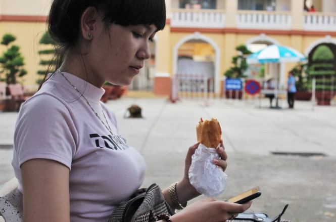 Lê Gia Thảo (Tây Ninh) ăn tạm bánh mì ngồi chờ đến 13g30 khi trường bắt đầu làm việc. Ảnh – Ngọc Tuyền
