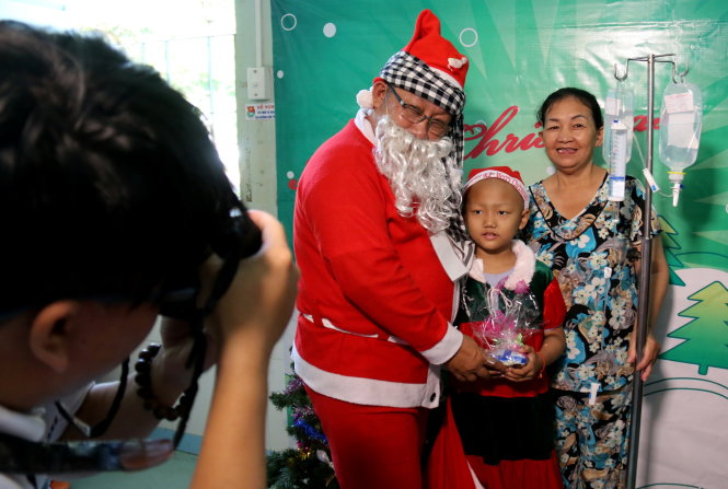 Bệnh nhi Nguyễn Hồ Ngọc Bích chụp hình cùng ông già Noel và bà ngoại dù tay vẫn phải truyền dịch - Ảnh: Ngọc Hiển