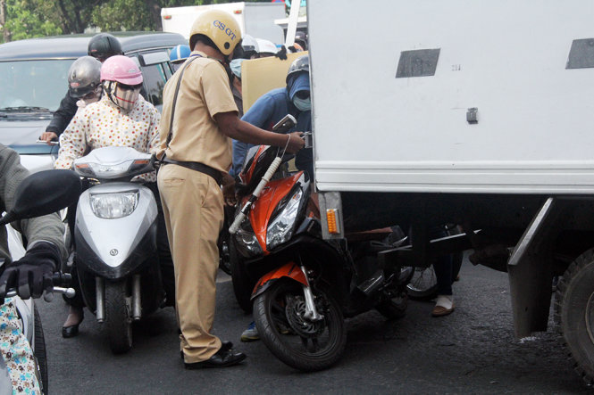 Cảnh sát giao thông giúp một phụ nữ bị ngã trong đám đông kẹt xe ở vòng xoay Dân Chủ - Ảnh: Q.Khải