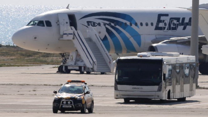 Xe buýt đưa các hành khách được thả rời sân bay. Phía sau là chiếc máy bay của hãng Egypt Air bị không tặc khống chế ngày 29-3- Ảnh: AP
