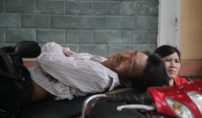 Một phụ huynh chợp mắt trên yên xe máy ở điểm thi Trường THPT Huỳnh Thúc Kháng, TP Vinh, Nghệ An - Ảnh DOÃN HÒA