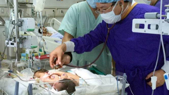 Ông Trần Bình Giang, phó giám đốc Bệnh viện Việt Đức, khám cho 2 bé song sinh dính nhau - Ảnh: L.ANH