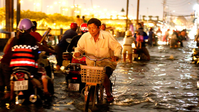 Một người đàn ông cố đạp xe đạp vượt qua dòng nước ngập - Ảnh: NGỌC DƯƠNG