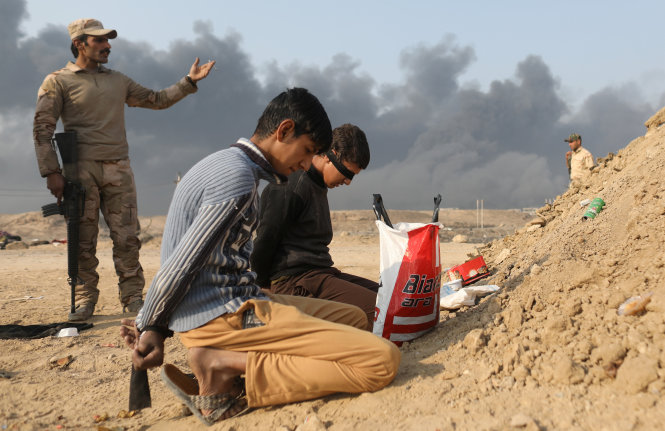 Một người lính Iraq đứng cạnh hai tù nhân được coi là chiến binh IS tại khu vực giao tranh phía nam thành phố Mosul, ngày 27-10 - Ảnh: REUTERS