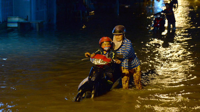 Chị Lê Thái Thanh cùng con dẫn xe chết máy trên đường ngập nước - Ảnh: HỮU KHOA