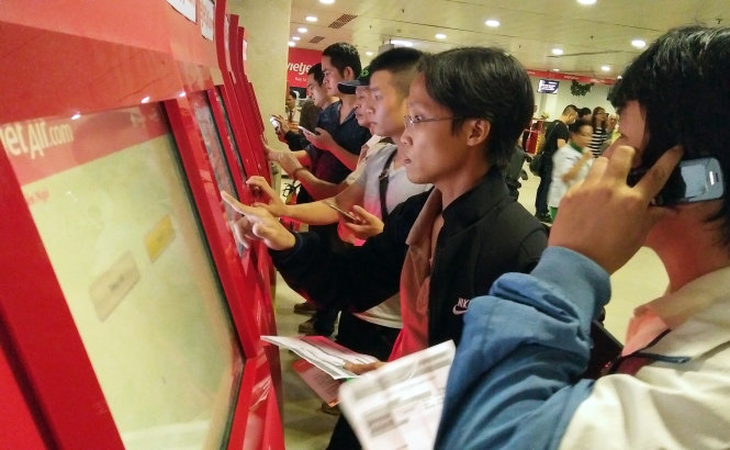 Nhiều hành khách phải tự làm thủ tục bay điện tử vì số lượng hành khách xếp hàng làm thủ tục bay quá đông tại sân bat Tân Sơn Nhất, TP.HCM chiều 28-12 - Ảnh: HỮU KHOA