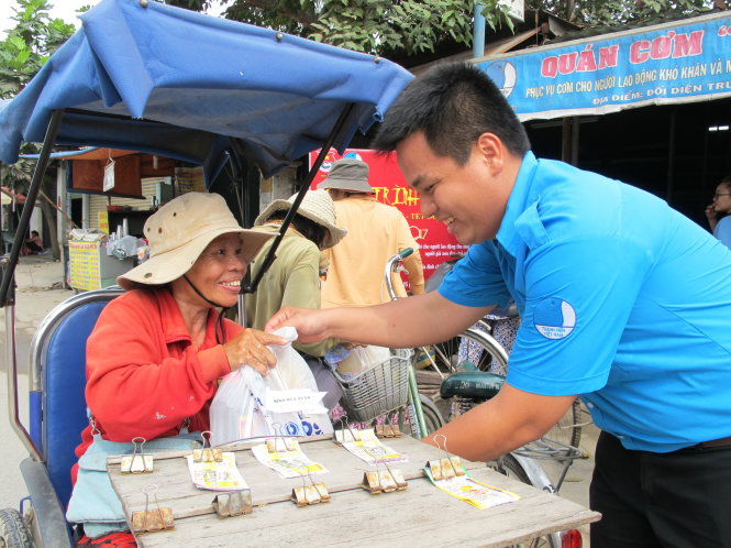 Bạn Phạm Hữu Lộc trao cơm và quà tết cho cô Hồng bán vé số - Ảnh: K.ANH