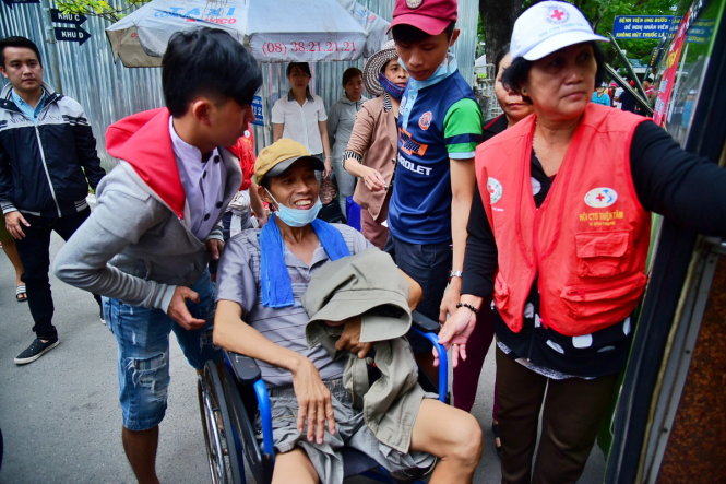 Bệnh nhân Phan Văn Hạ ngồi xe lăn được con trai cùng các tình nguyện viên của Hội Chữ thập đỏ chuẩn bị đưa lên xe - Ảnh: HỮU THUẬN