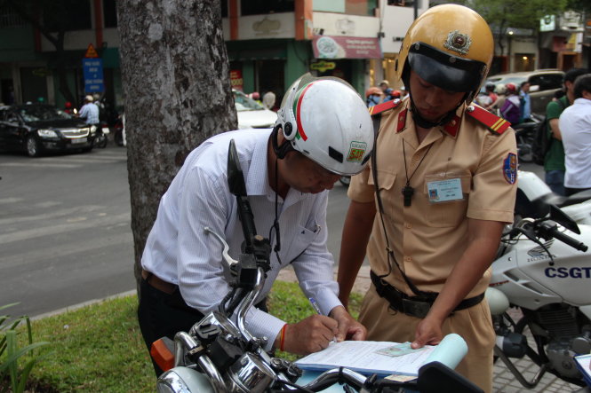 Một người chạy xe lên vỉa hè đường Nguyễn Trung Trực , Q.1 (TP.HCM) ký vào biên bản vi phạm - Ảnh: Lê Phan