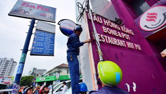 Nhân viên công ty công ích Q.1 tháo dỡ những tấm biển vi phạm trên vỉa hè đường Nguyễn Trãi - Ảnh: HỮU THUẬN