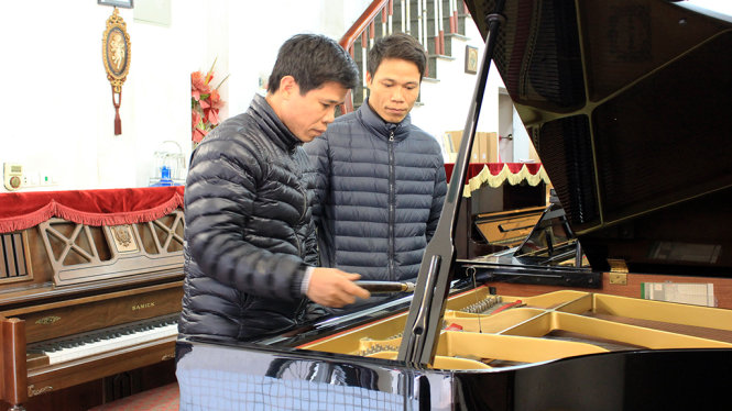 Thợ lên dây dương cầm Đỗ Văn Nhương (trái) và em trai của mình - cũng là một thợ lên dây - đang chăm sóc cho một cây dương cầm của khách hàng - Ảnh: HÀ THANH
