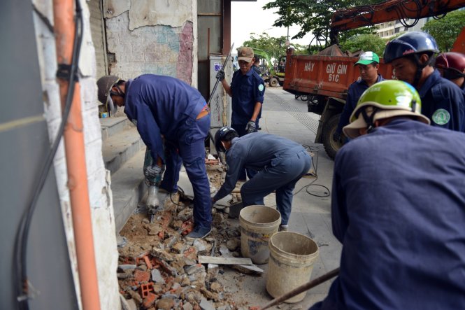 Các nhân viên công ích quận 1 tháo dỡ một công trình lấn vỉa hè vào chiều 19-3 - Ảnh: Lê Phan