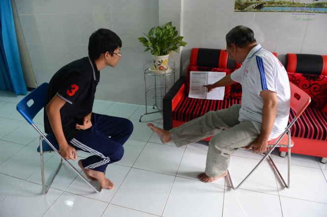 Ông Dũng cùng con trai đọc tài liệu hướng dẫn tập vật lý trị liệu tại nhà -
 Ảnh: QUANG ĐỊNH