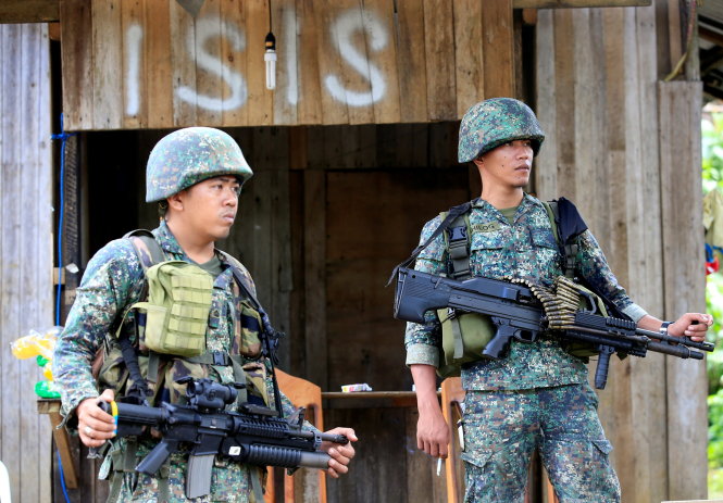 Binh sĩ Philippines canh giữ ở đường chính của làng Mapandi thuộc TP Marawi trong quá trình tiêu diệt khủng bố. Sau lưng họ là bảng chữ ghi tên tắt của lực lượng khủng bố Nhà nước Hồi giáo - Ảnh: Reuters