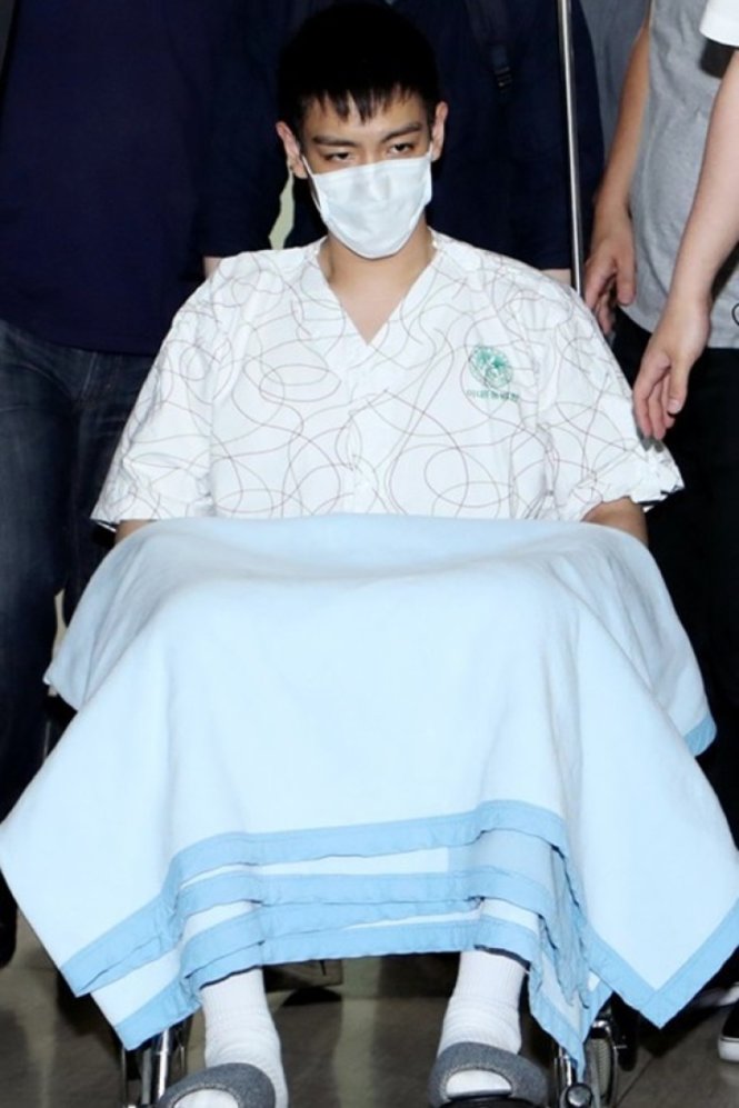 T.O.P xuất hiện trên xe lăn với khẩu trang và bộ trang phục bệnh nhân - Ảnh: On.cc