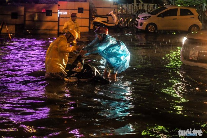 Một công nhân thoát nước đang giúp một người phụ nữ đi đường, sau khi chiếc xe máy bị đổ xuống nước - Ảnh: Nguyễn Khánh