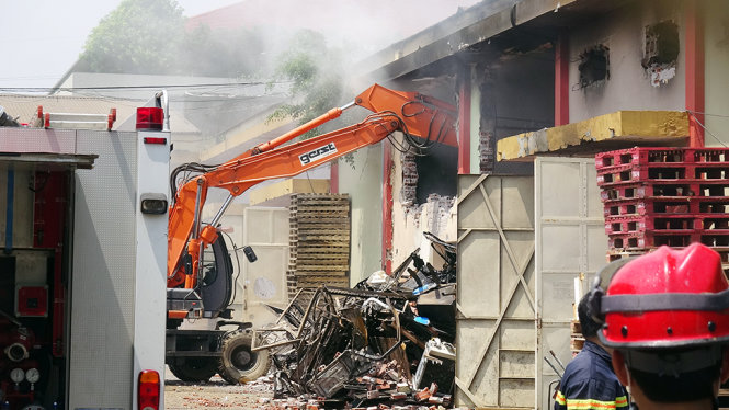 Để tiếp cận, dập tắt hoàn toàn đám cháy, lực lượng chức năng phải dùng máy xúc phá tường - Ảnh : CHÍ TUỆ