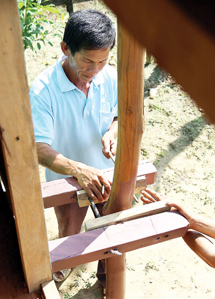 Ông Trần Trung Điệt hoàn thiện bộ phận trượt trên cột gỗ giữ cho ngôi nhà không bị xê dịch mà chỉ lên xuống
