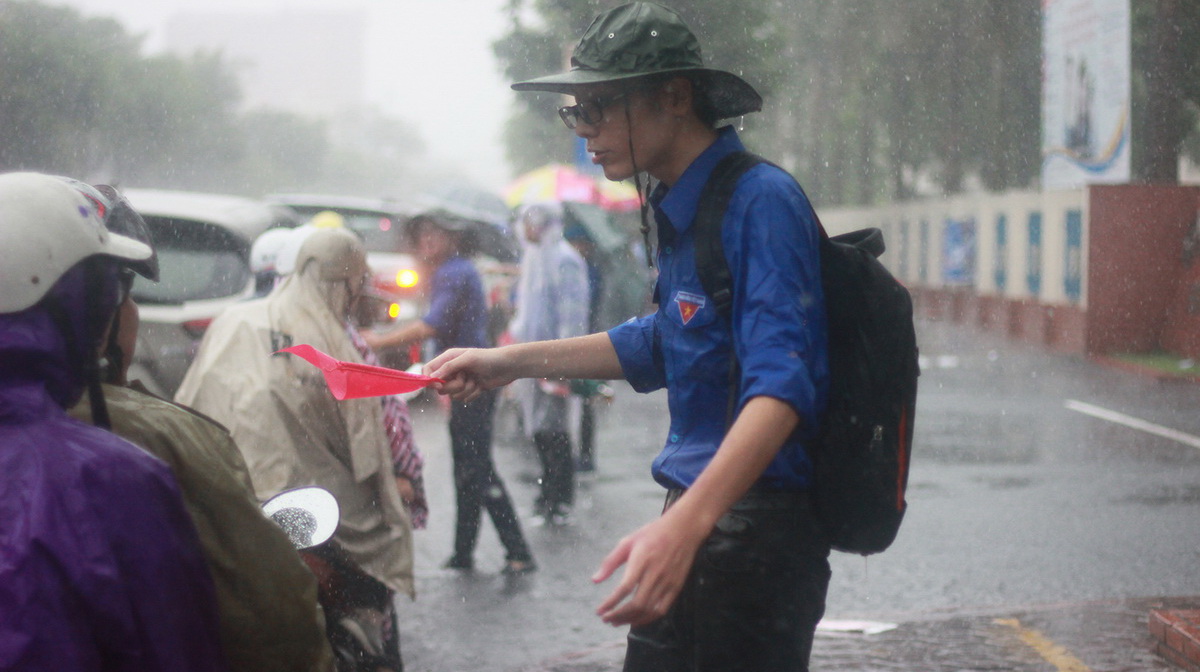 Nam sinh viên tình nguyện của trường Đại học Hàng Hải Việt Nam tại Hải Phòng đội mưa hướng dẫn người nhà và thí sinh đến làm thủ tục dự thi trong ngày 30-6 - Ảnh: TIẾN THẮNG