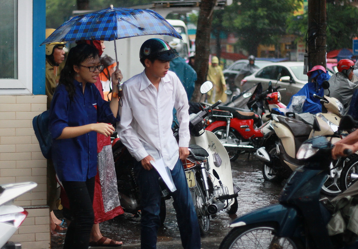 Một nữ sinh viên tình nguyện tại điểm thi trường ĐH Hàng Hải Việt Nam cầm ô che mưa cho thí sinh được người nhà đến đón trong trời mưa lớn - Ảnh: TIẾN THẮNG
