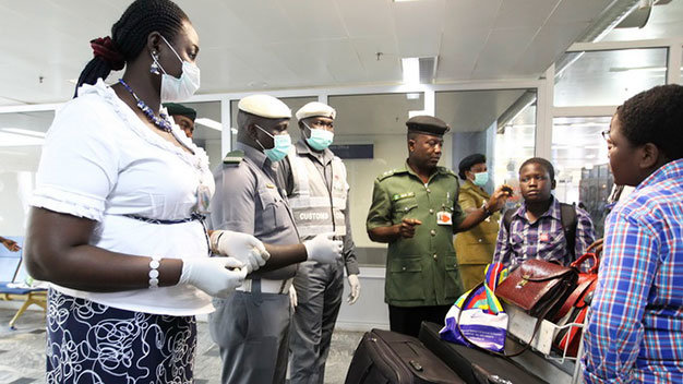 Nhân viên hải quan Nigeria đeo khẩu trang và găng tay để kiểm tra hành khách đến sân bay ở Abuja - Ảnh: Reuters