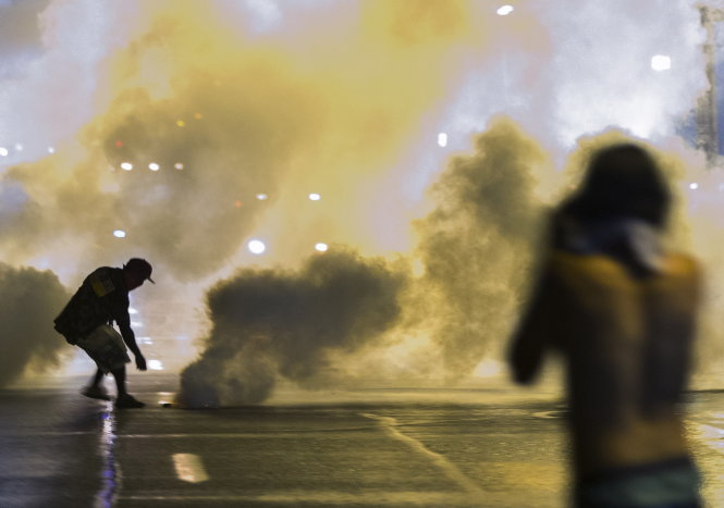 Người biểu tình nhặt lựu đạn khói ném trả lại cảnh sát - Ảnh: Reuters