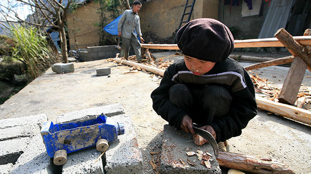 Hà Giang: Em bé dân tộc ở bản Sủng Là (Hà Giang) cắt khoanh gỗ tròn để làm bánh xe cho chiếc ôtô từ bình nhựa đựng dầu xe máy bỏ đi - Ảnh: Lê Bích