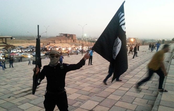 Một chiến binh IS cầm vũ khí và giương cờ của tổ chức này - Ảnh: Reuters