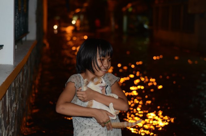 Em Lê Thị Ngọc Hân, 11 tuổi, chơi với chú mèo của mình trong dòng nước ngập - Ảnh: T.Tùng