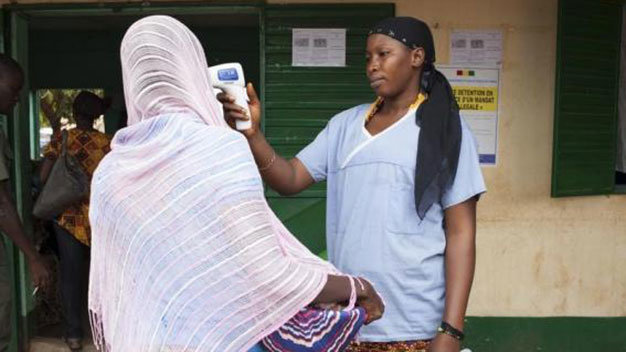 Một nhân viên y tế kiểm tra thân nhiệt của một phụ nữ rời Guinea ở biên giới với Mali ngày 2-10-2014 - Ảnh: Reuters 