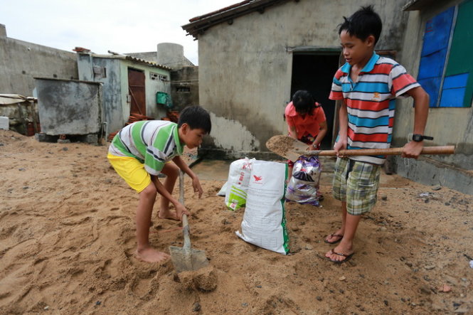 Em Đào Đức Quý (phải) và Ngô Đức Cẩn phụ giúp gia đình đóng bao tải cát chống bão - Ảnh: Tiến Thành