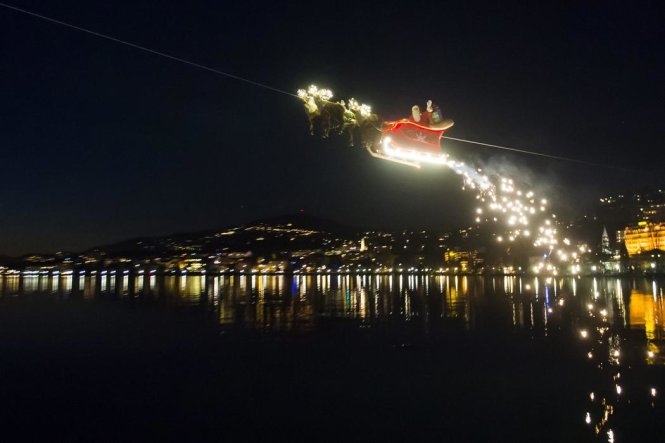 Trong khi đó, ông già Noel điều khiển cỗ xe với đàn tuần lộc có màn trình diễn ngoạn mục vẫy tay chào mọi người từ trên không ở khu vực hồ Geneva, Thụy Sĩ - Ảnh: EPA