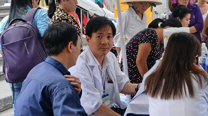 Ông Huy (áo Blouse trắng)  tự xưng là bác sĩ của bệnh viện Nhân Dân 115 đang khám bệnh cho người dân tại chợ Phú Nhuận, Q.Phú Nhuận, TP.HCM - Ảnh: Hữu Khoa