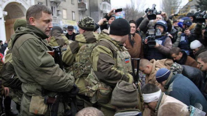 Binh sĩ Ukraine bị buộc quỳ gối trước hiện trường cuộc tấn công xe buýt điện - Ảnh: AFP