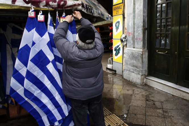 Một người bán hàng trên phố đang gắn mác giá lên các quốc kỳ Hy Lạp treo bán tại gian hàng ở Athens - Ảnh: Reuters 