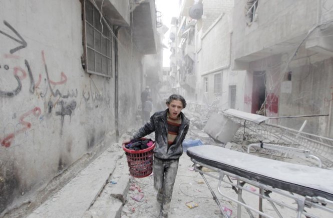 Một cậu bé mang đồ đạc của mình chạy khỏi địa điểm bị đánh bom ở quận Aleppo's al-Fardous, Syria ngày 2/4/2015. Các nhà hoạt động cho rằng sự việc được gây ra bởi các lực lượng trung thành với Tổng thống Syria Bashar al-Assad - Ảnh: Rami Zayat