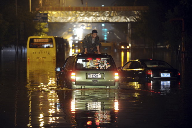 Một người đàn ông ngồi trên mui xe hơi bị chết máy do nước lũ dâng cao tại tỉnh Cát Lâm - Ảnh: Reuters