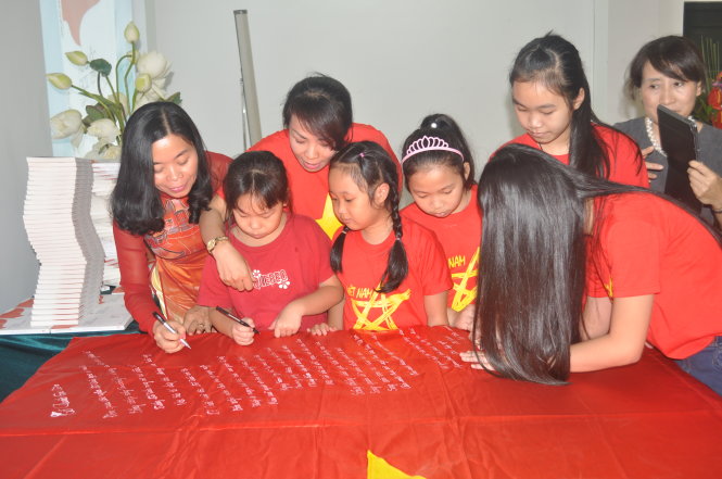 Nhà thơ Nguyễn Phan Quế Mai (bìa trái) cùng các em thiếu nhi ký tên trên lá cờ Tổ quốc có in bài thơ Tổ quốc gọi tên mình để gửi tặng các chiến sĩ Trường Sa - Ảnh: V.V.Tuân