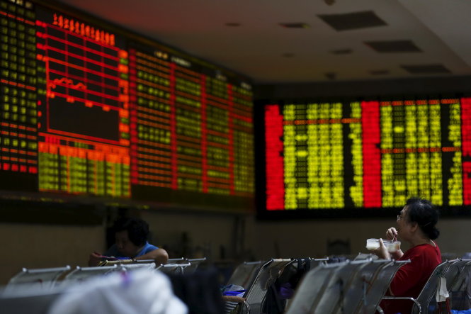 Một nhà đầu tư tranh thủ ăn trưa trước bảng điện tử chứng khoán rực đỏ ở Thượng Hải ngày 8-7 - Ảnh: Reuters
