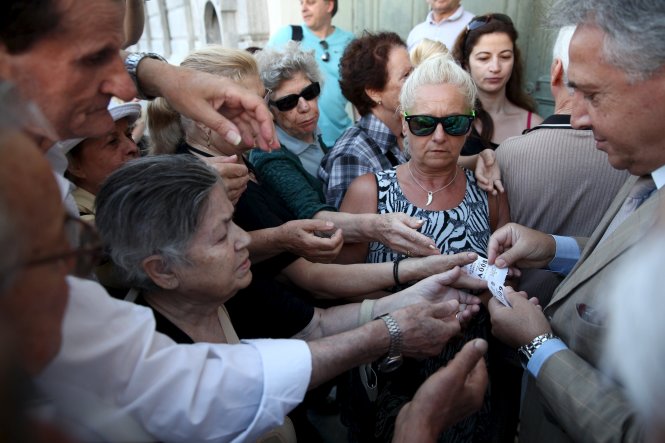 Người dân Hi Lạp ở thủ đô Athens lấy số thứ tự từ một quản lý chi nhánh Ngân hàng Nhà nước để chờ nhận tiền lương hưu hôm 13-7 - Ảnh: Reuters