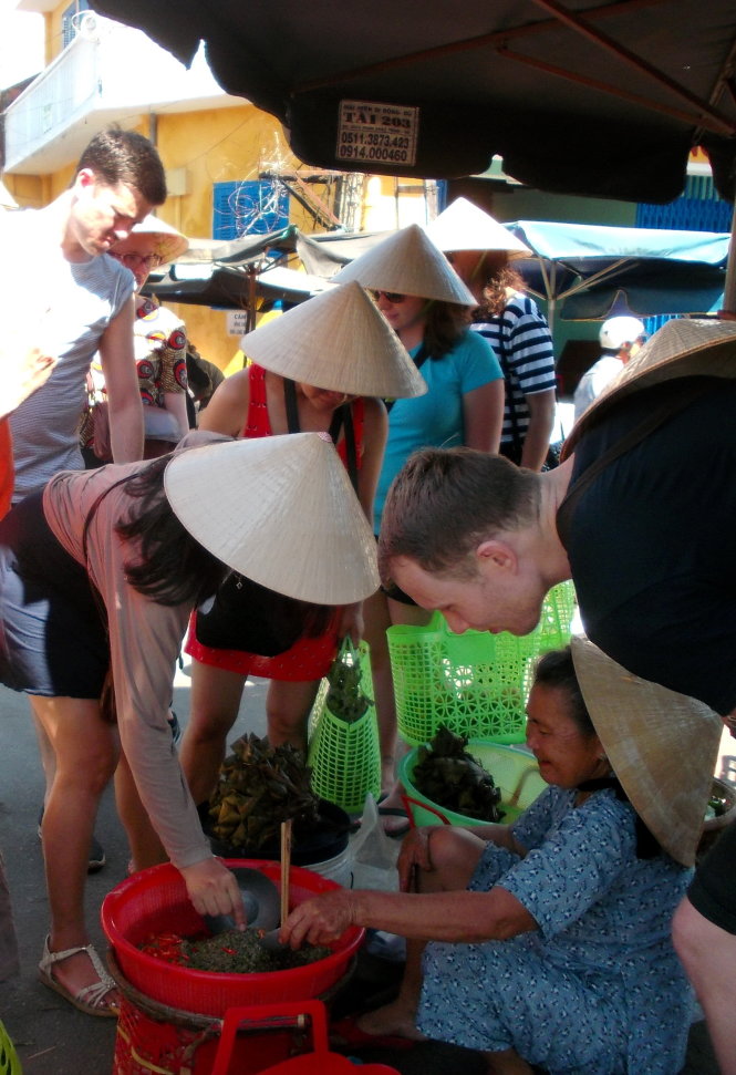 Một nhóm du khách nước ngoài  mang theo giỏ xách, đội nón lá  dạo qua chợ Hội An