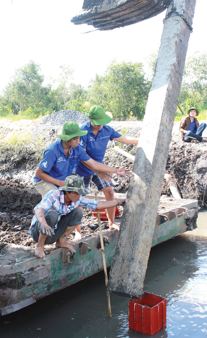 Chiếc cọc thứ nhất đã đóng xuống lòng kênh nhưng mất rất nhiều thời gian chiếc cọc thứ hai vẫn chưa vào khớp. Trong ảnh là hai đồng đội của chúng tôi Quang Huy và Hồng Anh (Trường ĐH Bách khoa, ĐHQG TP.HCM) nhảy xuống chiếc xáng cạp cùng phụ với hai người thợ điều khiển máy Kobe cố gắng định vị để nối chiếc cọc thứ hai vào khớp nối trước khi đóng cố định xuống lòng kênh tại công trình xây cầu ở xã Bình Mỹ, Củ Chi (TP.HCM) - Tác giả: Minh Dũng (xã Bình Mỹ)