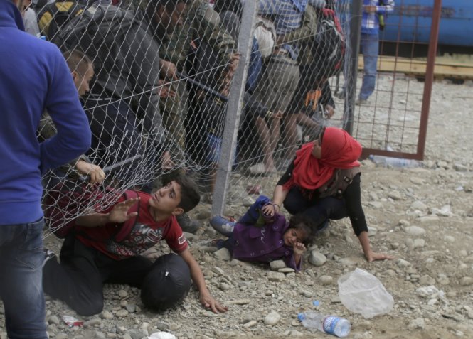 Cảnh sát ở Macedonia đang cố gắng ngăn chặn những người di cư chui dưới hàng rào để tìm cách lên tàu tại một nhà ga ở Gevgelija - Ảnh: Reuters