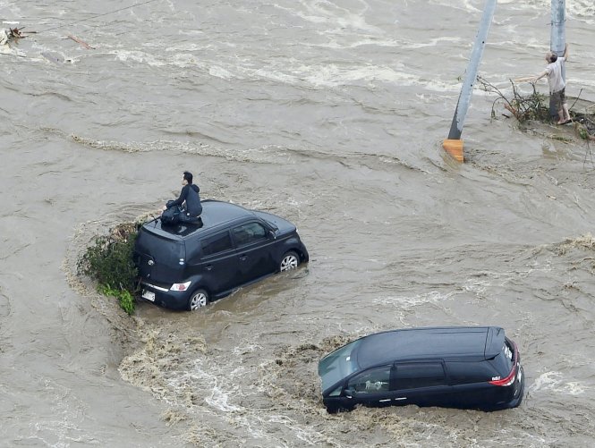 Một người trên nóc xe hơi (trái) và một người khác bám cột điện chờ được cứu hộ ở Joso. Ảnh: Reuters