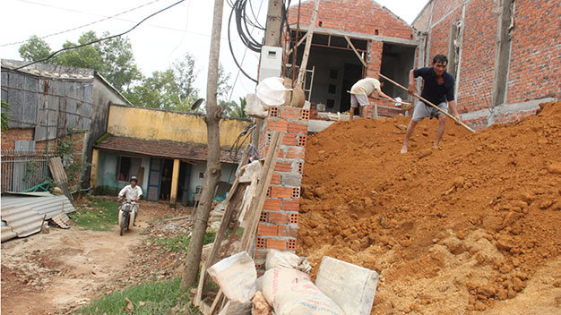 Nóc một nhà dân (bên trái) chỉ cao bằng nền nhà một hộ dân thực hiện chỉnh trang nâng cốt nền bằng mặt đường dẫn cầu Kỳ Phú 1 và Kỳ Phú 2 - Ảnh: Trường Trung