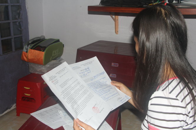 Chị Nguyễn Thị Châu Trân xem lại hóa đơn tiền điện và thư xin lỗi của Công ty Điện lực Bình Phú - Ảnh: Quang Khải