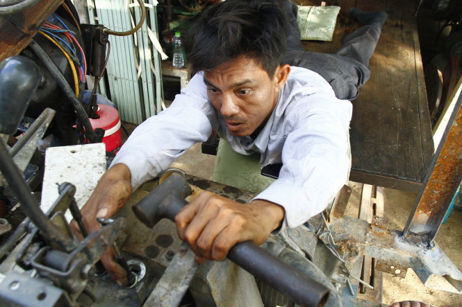 Anh Nguyễn Văn Thông cố dùng hết sức đôi tay của mình để sửa chữa máy móc dù phải nằm trên phản gỗ   - Ảnh: Xuân An