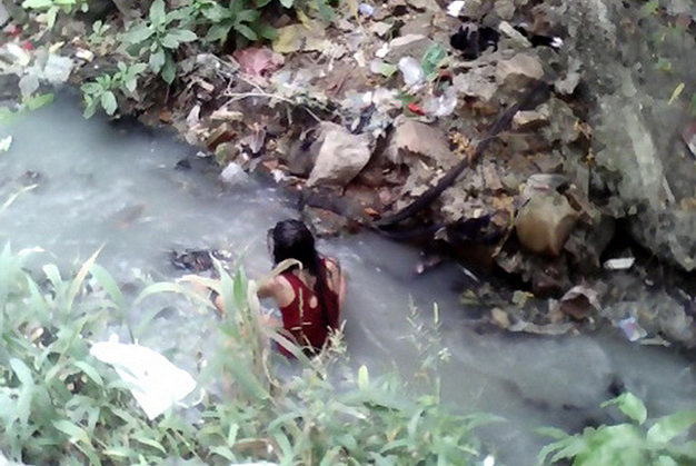 Cô gái ngồi bệt dưới mương nước trước khi chui vào cống - Ảnh: Người dân cung cấp